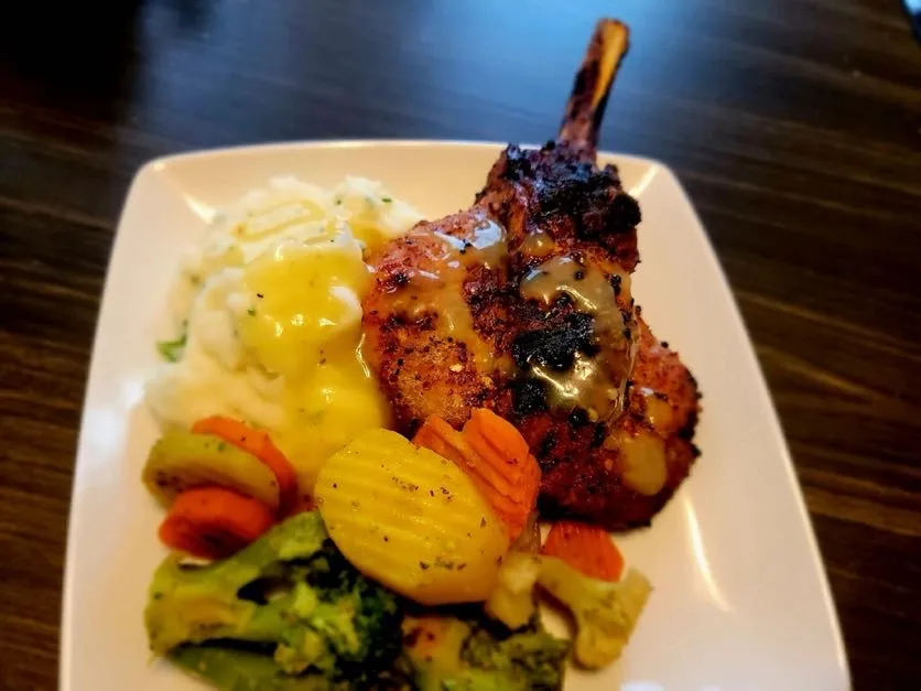Plated grilled pork chop with mashed potatoes and seasonal vegetables